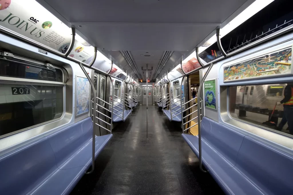 Interior de um vagão do metrô de Nova York com assentos azuis e estrutura metálica moderna

