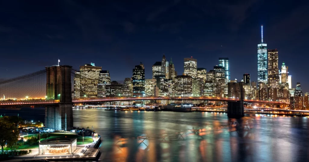 Ponte do Brooklyn à noite com Manhattan iluminada e reflexos no East River
