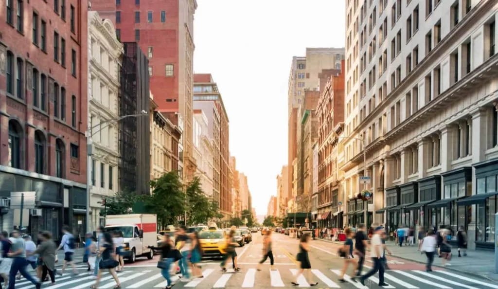 Rua movimentada em Manhattan com faixa de pedestres, táxis amarelos e prédios históricos