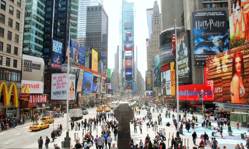 Times Square durante o dia, com pedestres, táxis amarelos e grandes painéis digitais
