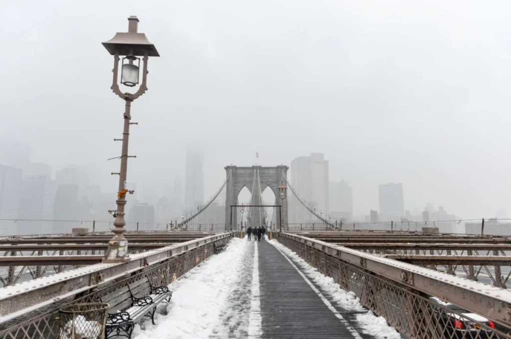 Ponte do Brooklyn coberta de neve com nevoeiro e skyline de Nova York ao fundo, inverno em Nova York, ponto turístico Brooklyn Bridge no inverno
