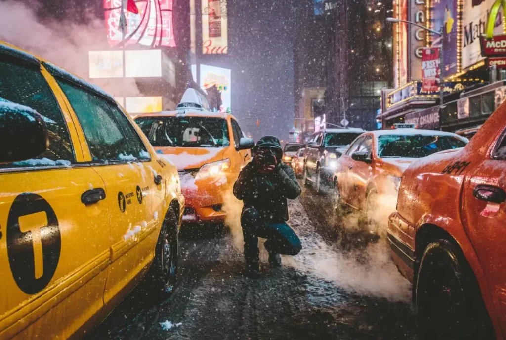 Times Square em Nova York com táxis amarelos e fotógrafo durante neve à noite, inverno em NYC, cidade iluminada com neve caindo
