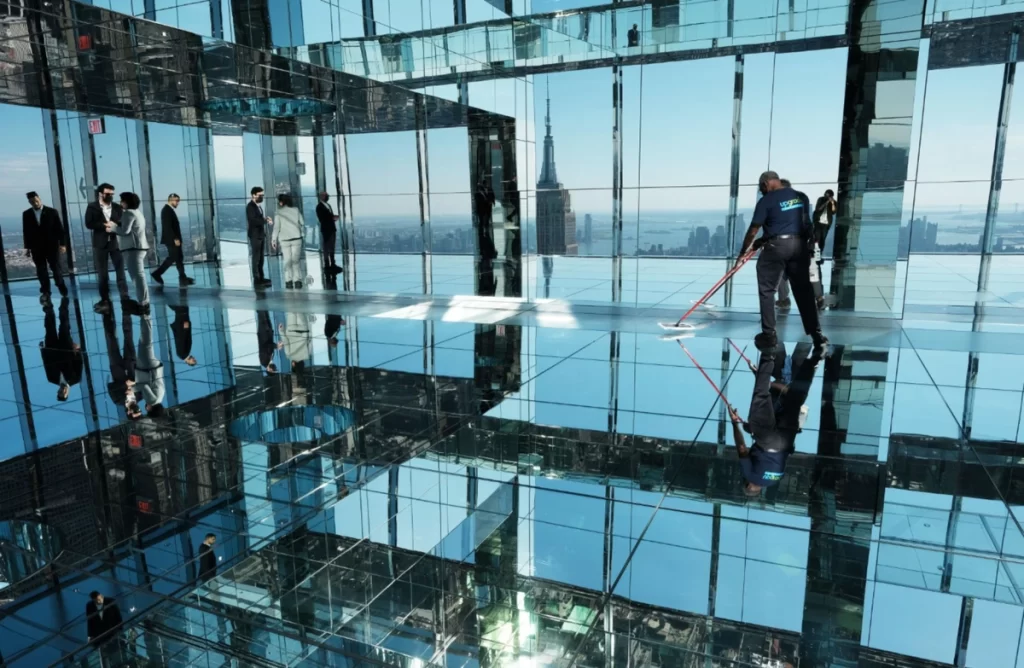 Sala espelhada do Summit One New York com vista para o Empire State Building e reflexos infinitos em Manhattan.