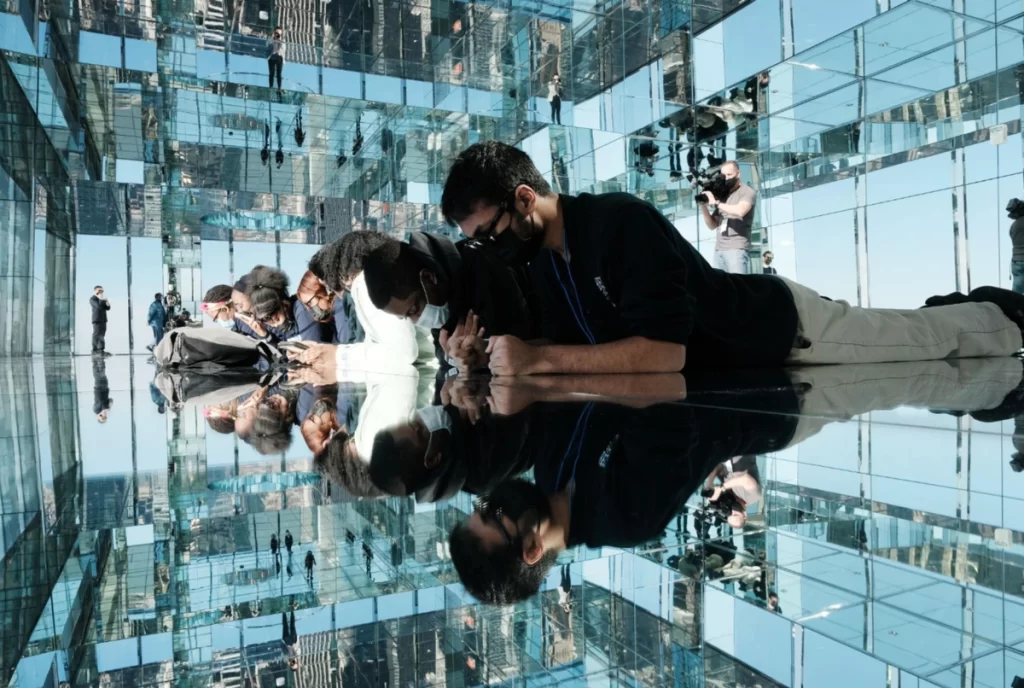 Visitantes explorando sala espelhada imersiva no Summit One New York com reflexos da cidade.