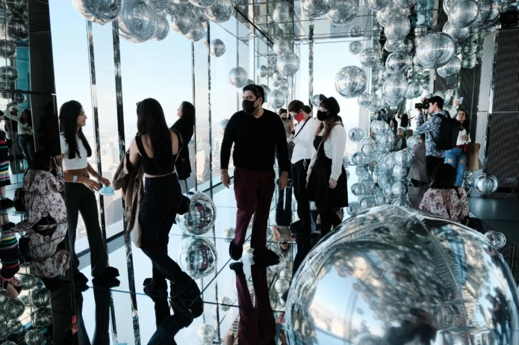 Visitantes explorando a sala espelhada com esferas flutuantes no Summit One New York.
