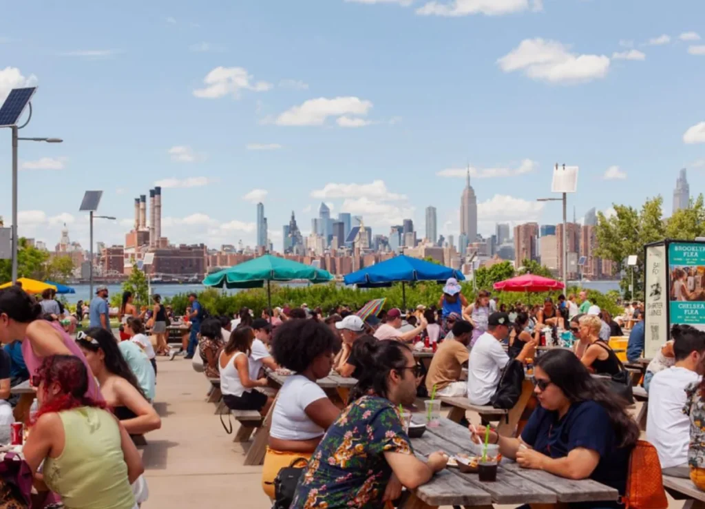 Área gastronômica movimentada no waterfront do Brooklyn com vista para Manhattan.