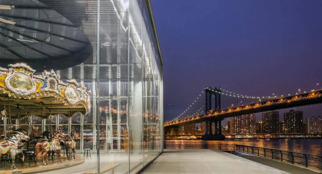 Jane's Carousel iluminado junto à Manhattan Bridge durante a noite em DUMBO, Brooklyn.