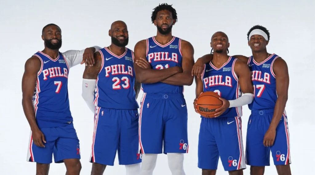 Jogos Philadelphia 76ers - Jaylen Brown, LeBron James, Joel Embiid e Tyrese Maxey aparecem reunidos em uma imagem ilustrativa do Philadelphia 76ers, vestindo o tradicional uniforme azul da franquia da Filadélfia. A montagem reúne grandes estrelas do basquete da NBA, incluindo atletas que não fazem parte do elenco oficial dos 76ers.